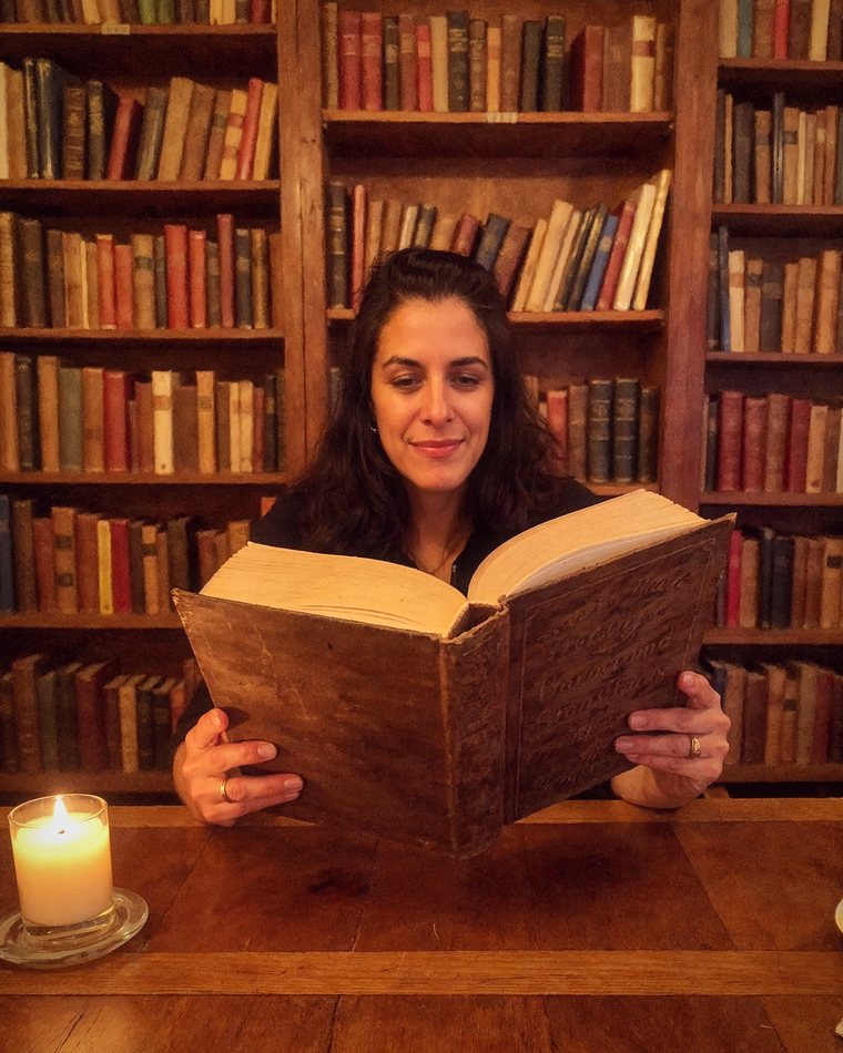 Lore Ferreyra leyendo un libro antiguo a la luz de una vela